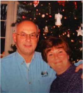 Dan ’70 and Edwina Amoroso similing at the camera with a Christmas tree behind them.