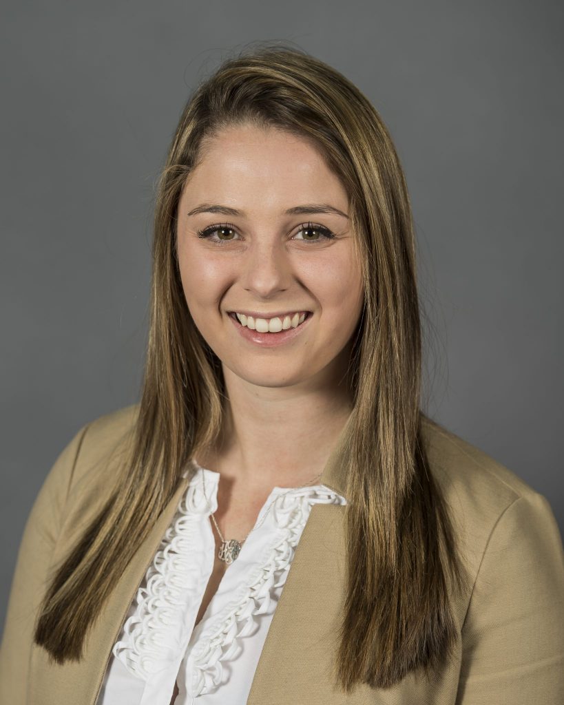 Allison Frankil is smiling in front of a grey background. She is wearing a beige cardigan with a white blouse and necklace.