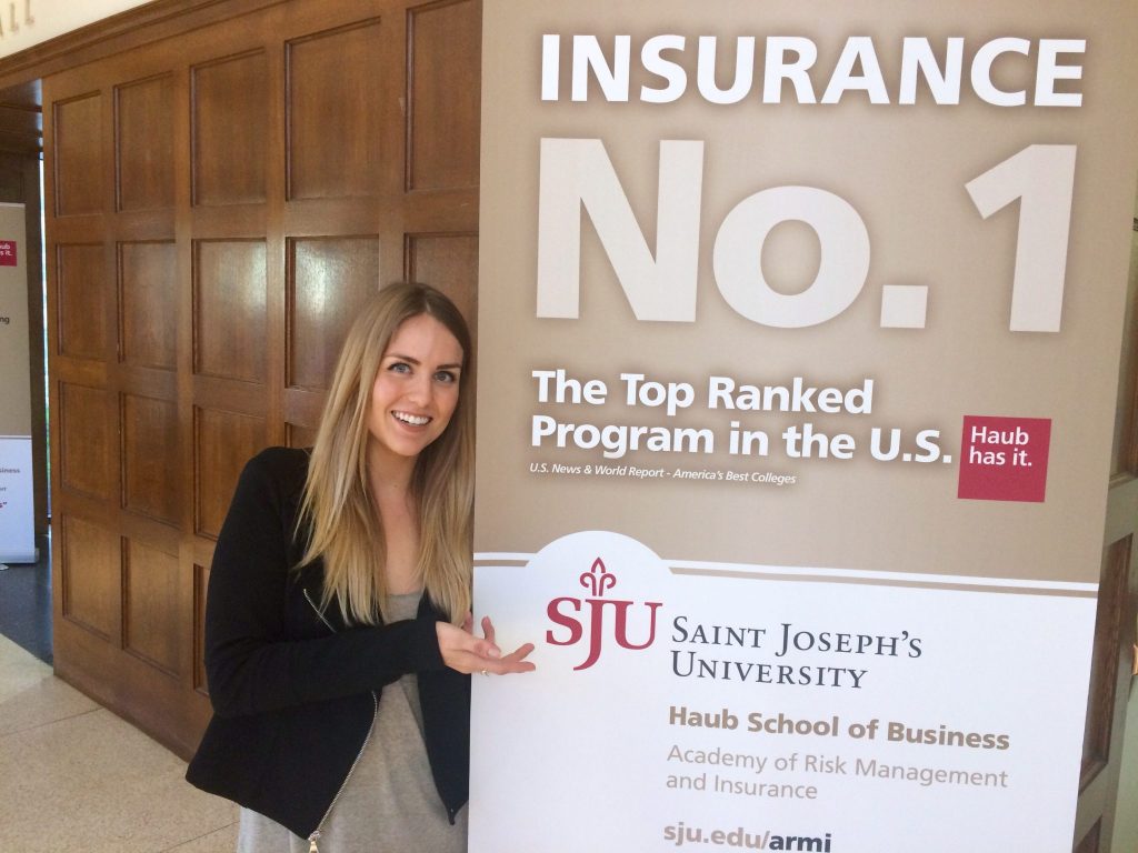 Katie Boutin is pointing to a sign reading, "Insurance No.1: The Top Ranked Program in the U.S.: Saint Joseph's University Haub School of Business."