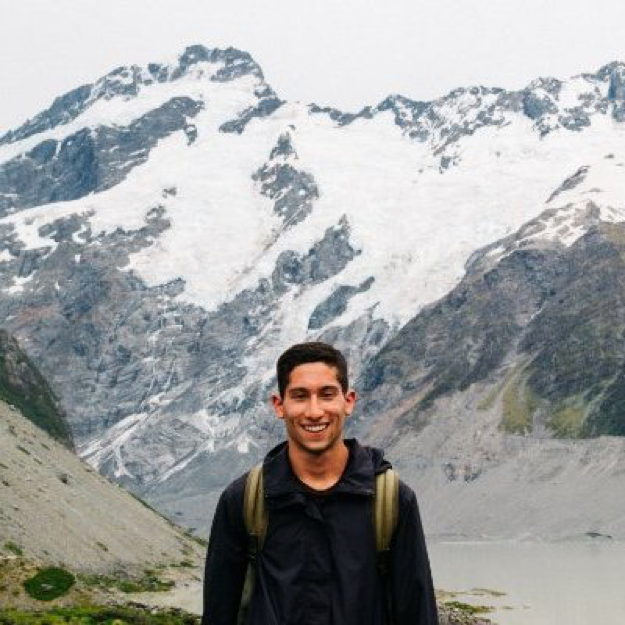 Michael Carnevale is smiling in front of a snowy mountain range with a backpack on.