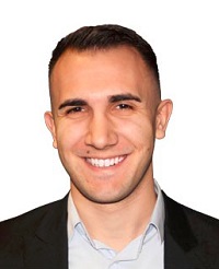 Chris Savino is smiling in front of a white background. He is wearing a dark suit with a light shirt.
