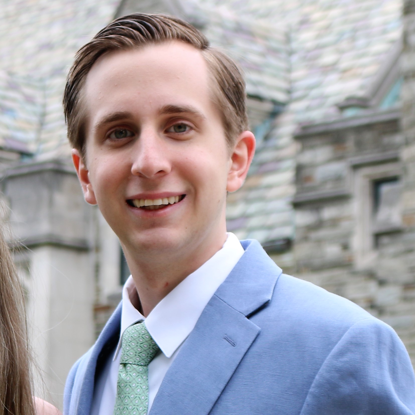 Joseph Wutkowski is smiling in front of barbell in a light grey suit and pale green tie.