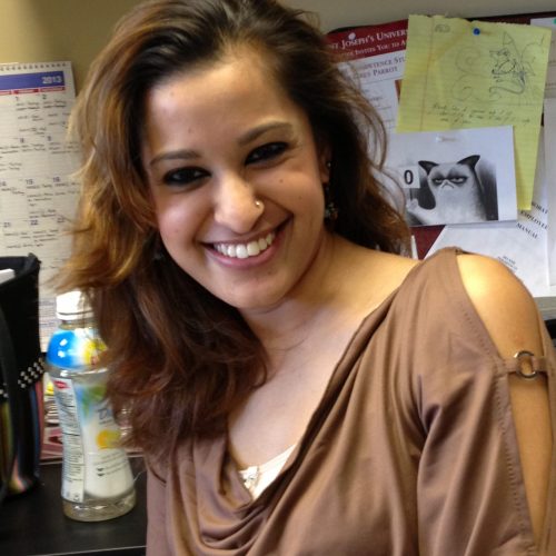 Mamatha Chary is smiling in an office cubicle. She has wavy, dark hair and is wearing a light brown blouse draped around her shoulders.