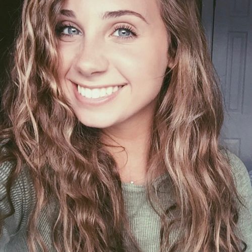 Alexa Sinatore has wavy, light hair and blue eyes. She is wearing a pale green top in a dimly lit room.