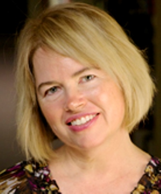 Gayle Sherman, a woman with blonde hair, is wearing a floral dress in front of a dark background.