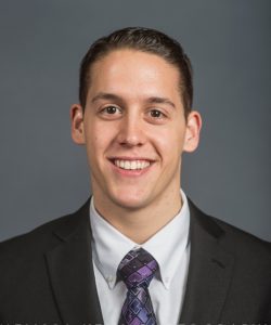 Louis Andreacchio, a young man with dark hair, smiles in front of a grey background in his suit and purple, patterned tie.