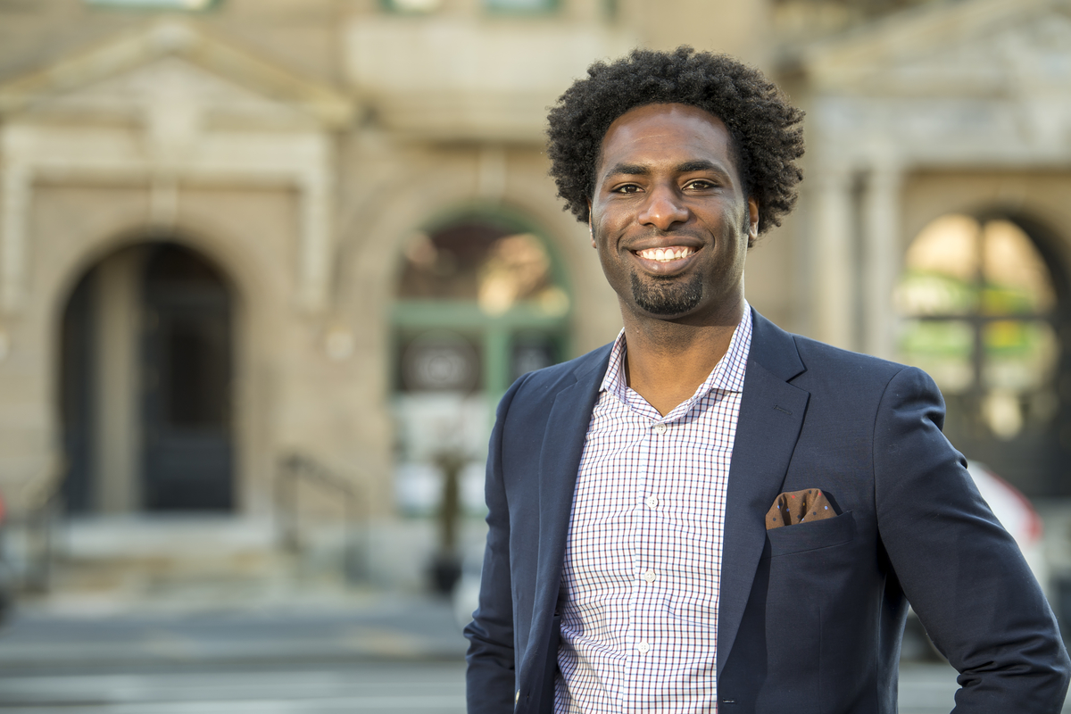 Jameel stands in front of a buidling wearing a blazer.