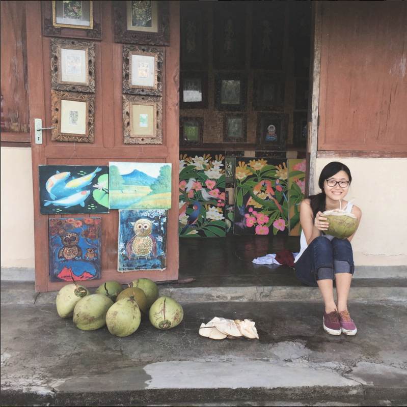 Dawn sits holding a large fruit by a collection of art.