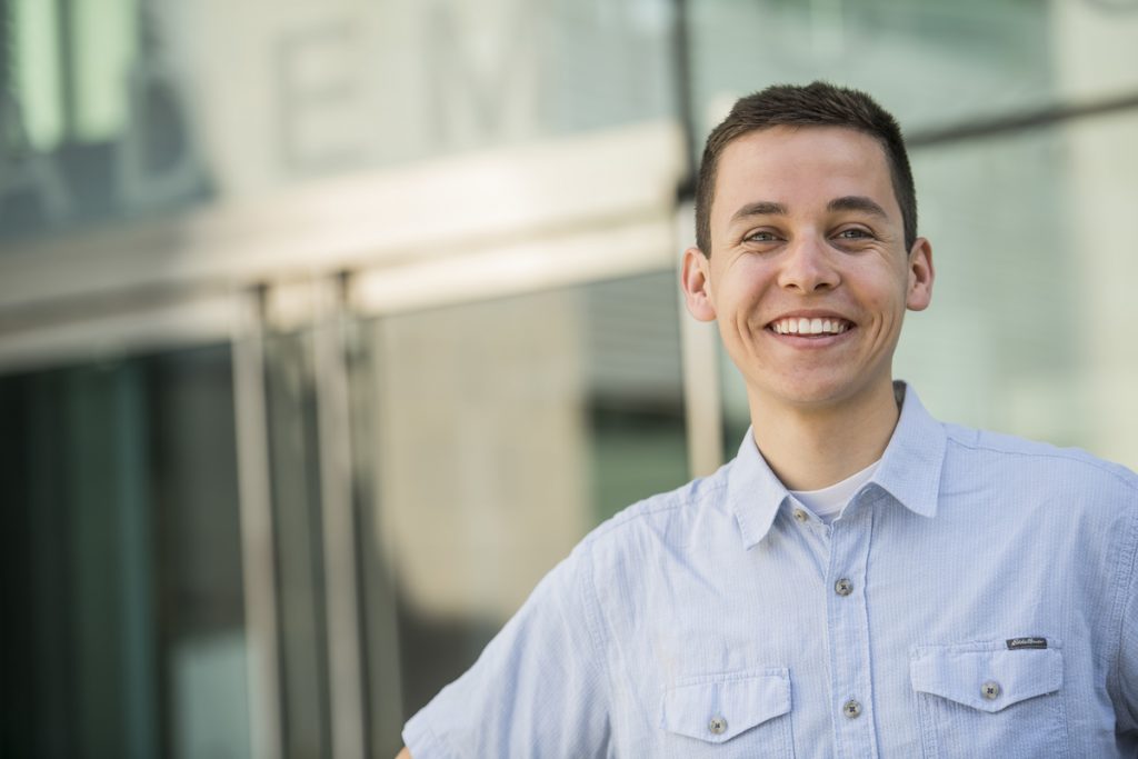 Dan smiles in front of a glass building.