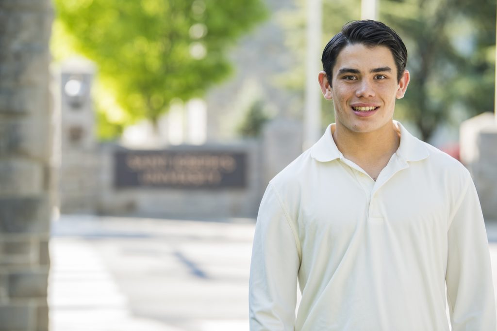 Chris, in a white button down, smiles with the Saint Joseph's sign in the background